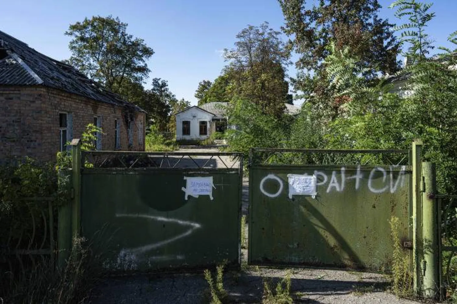 
A gate stands in front of a former health clinic, background center, that had been used by Russian soldiers in Izium, Ukraine, Wednesday, Sept. 21, 2022. (AP Photo/Evgeniy Maloletka)
