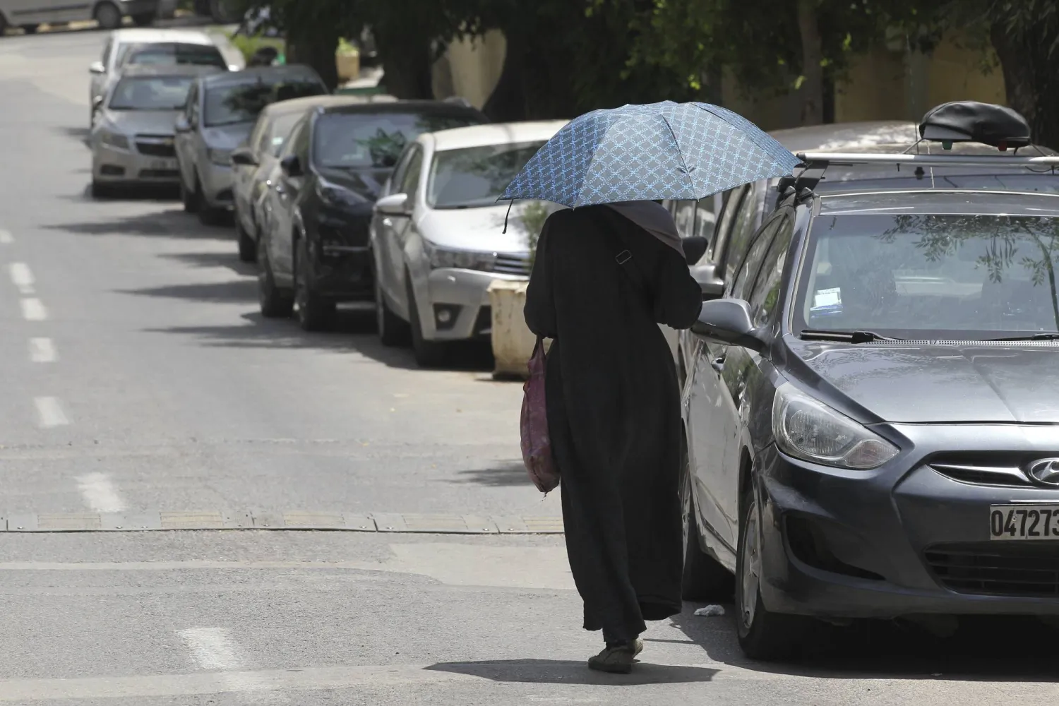 A woman shelters from the sun as she walks down a street in Algiers, Algeria, during a heat wave Tuesday, July 18, 2023. (AP Photo/Fateh Guidoum)