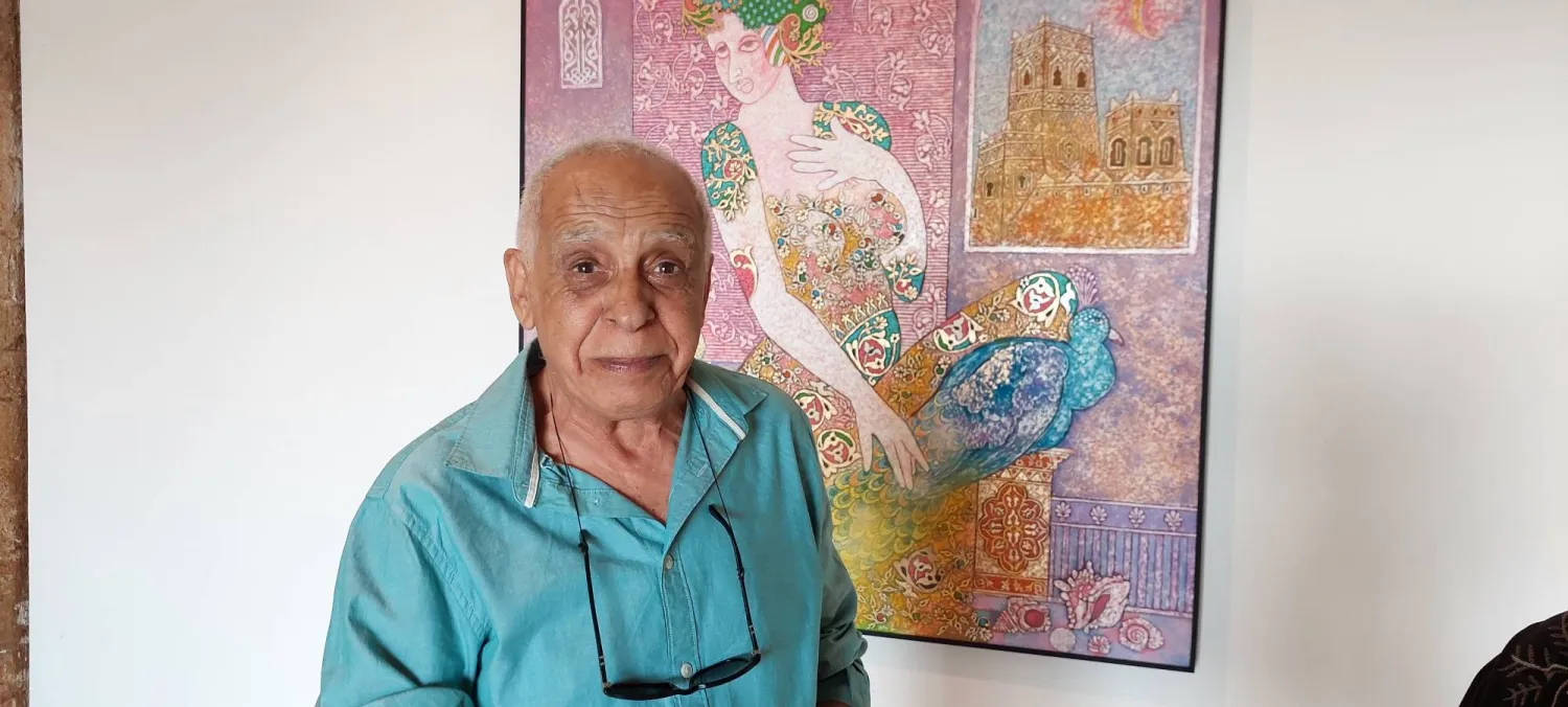 عزيز السيد وخلفه إحدى لوحاته (الشرق الأوسط)