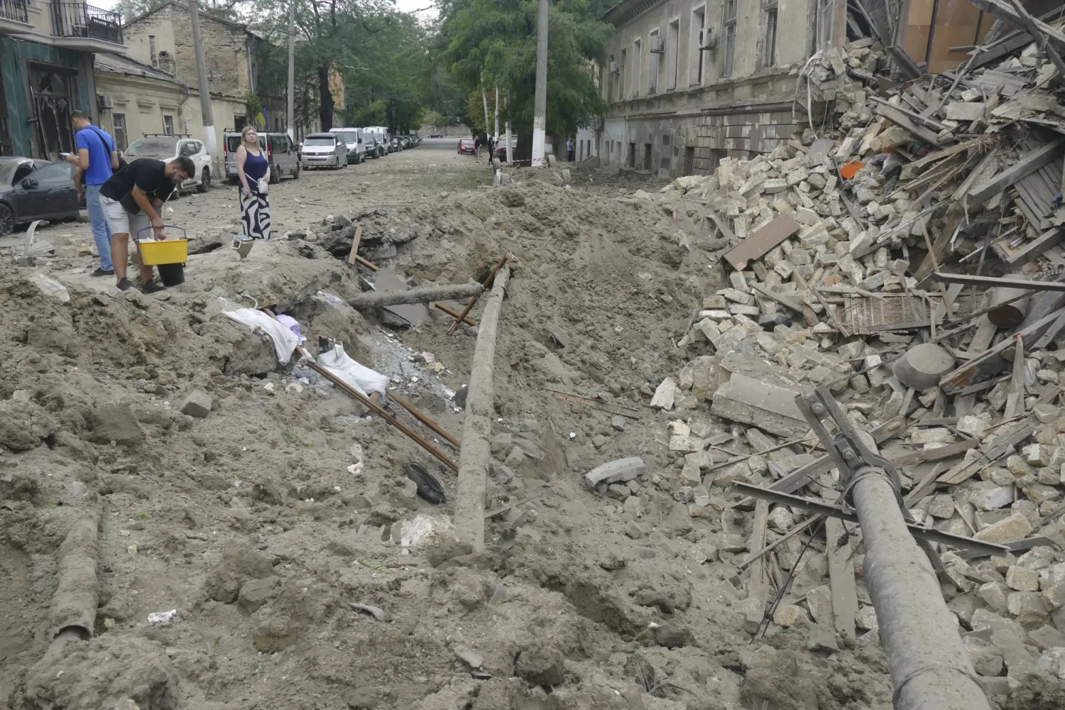 مواطنون أوكرانيون يقفون بجوار الأنقاض والدمار الذي لحق بمنطقة سكنية جراء القصف الروسي في أوديسا جنوب أوكرانيا في 23 يوليو 2023 (إ.ب.أ)