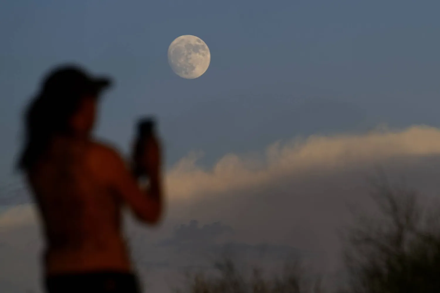 سيدة تلتقط صورة للقمر وسط الغيوم في فينيكس (أ.ب)