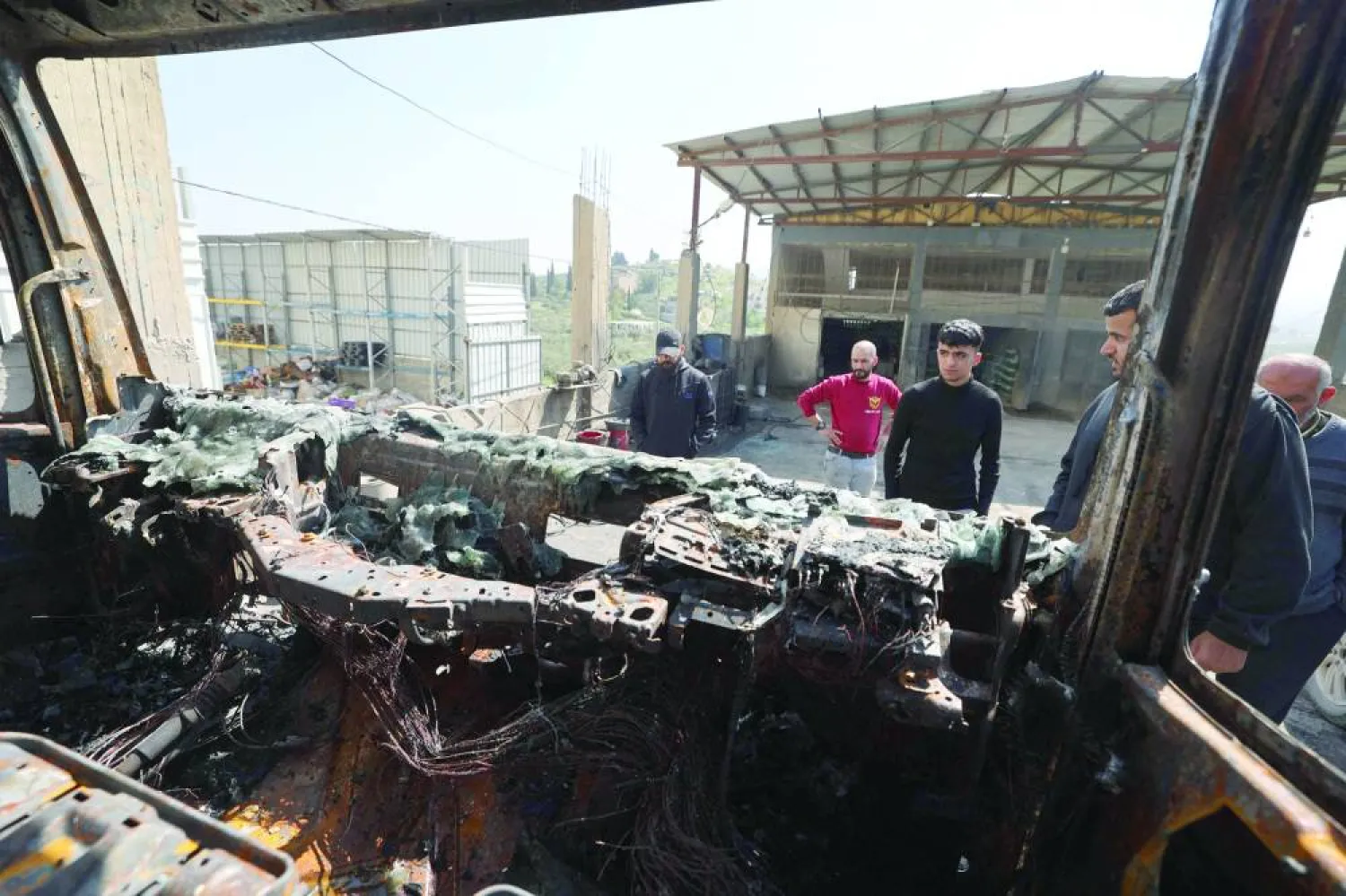 فلسطينيون يتفقدون سيارة محترقة في أعقاب هجوم مستوطنين على بلدة حوارة مارس الماضي (أ.ف.ب)