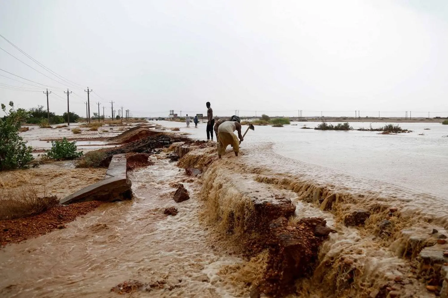 People dig a trench to evacuate muddy flood water along a street, following torrential rain in Saqqai near Omdurman on August 5, 2023. (AFP)