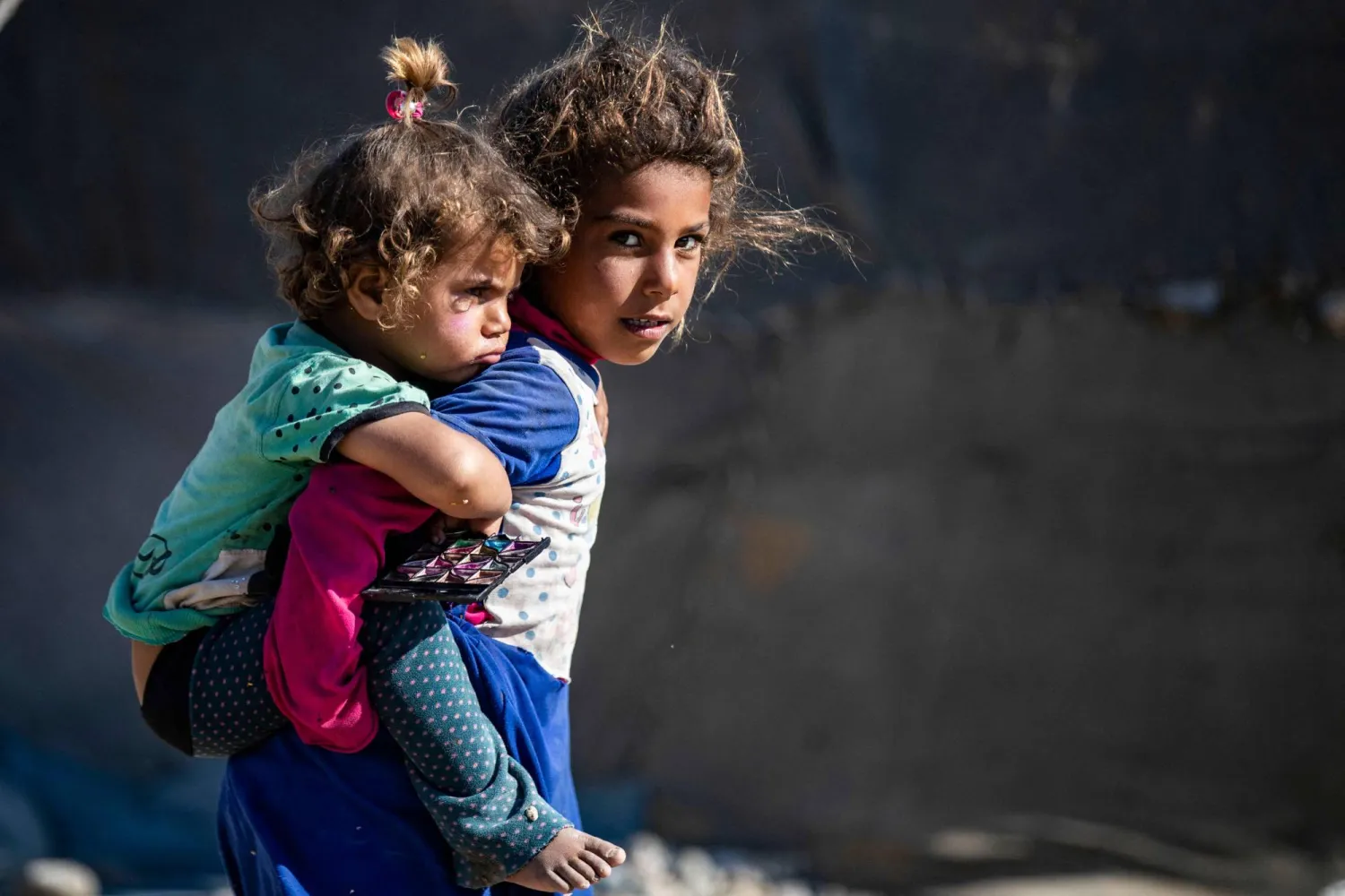 فتاة تحمل طفلة في المخيم اليوناني في الرقة بسوريا (أ.ف.ب)