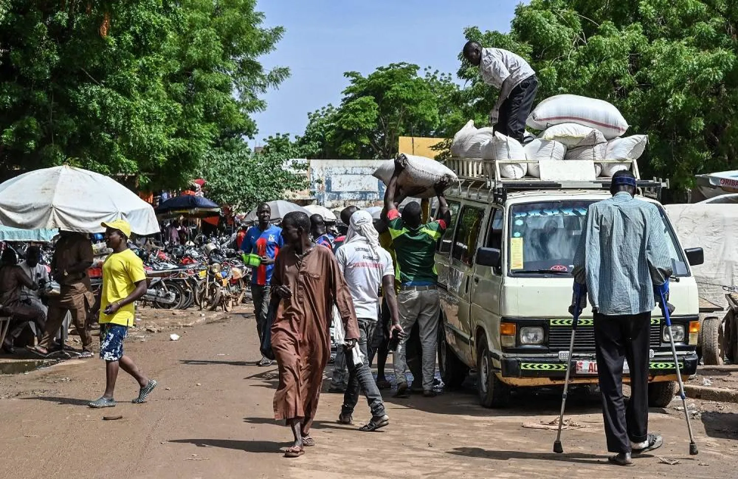 Men load bags of merchandise on a minivan as customers walk through Niamey's main market on August 8, 2023. (AFP)