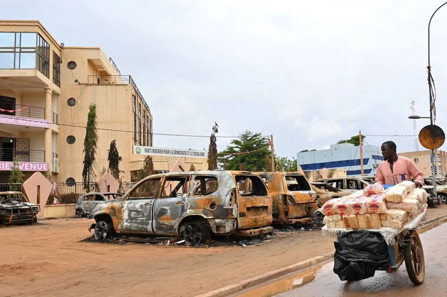 A street vendor pushes his cart past burned cars outside the headquarters of President Bazoum's Nigerien Party for Democracy and Socialism in Niamey on August 7, 2023. (AFP)