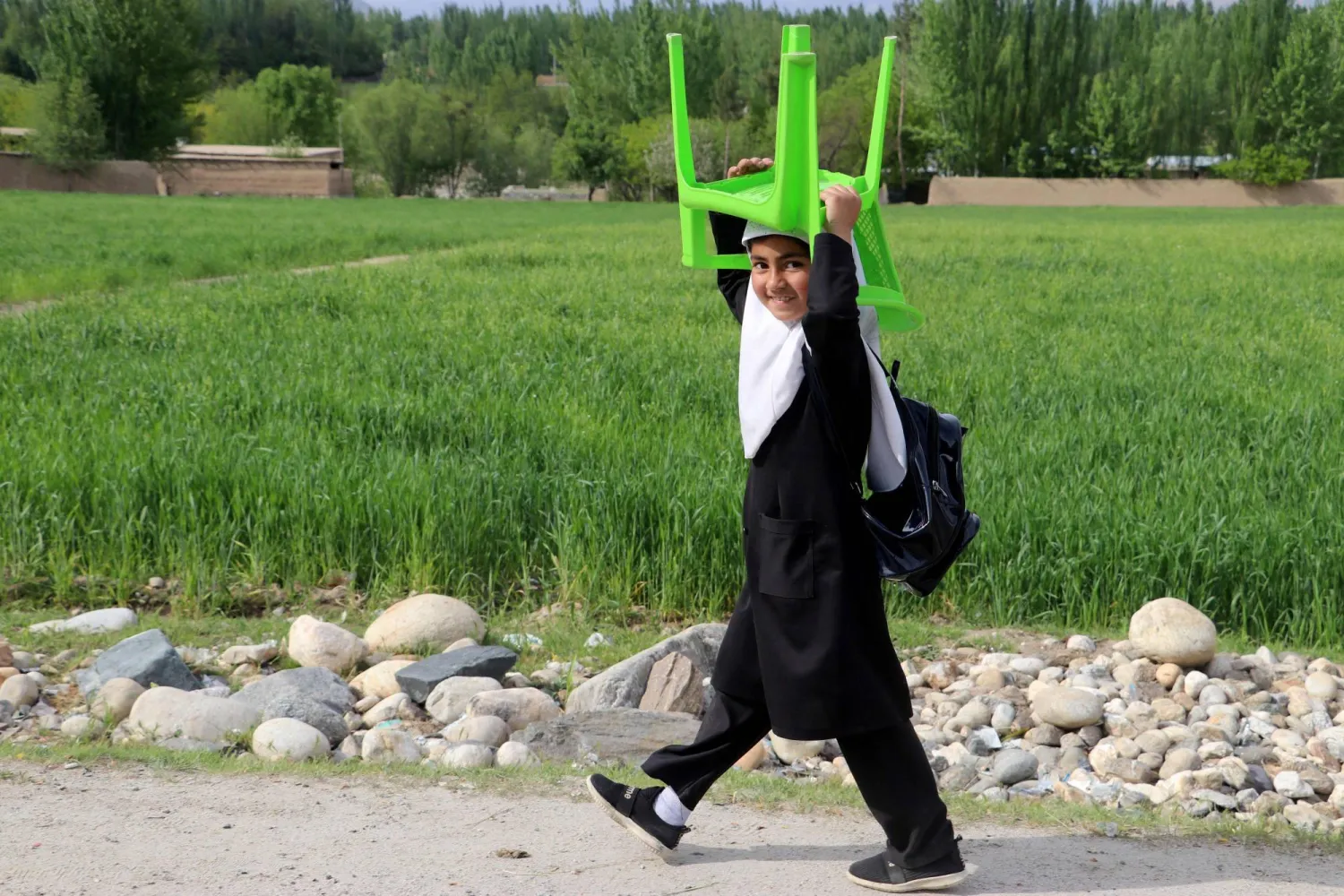 صورة أرشيفية لطالبة أفغانية تحمل كرسيها وحقيبتها الدراسية قبل حكم طالبان (أ.ف.ب)