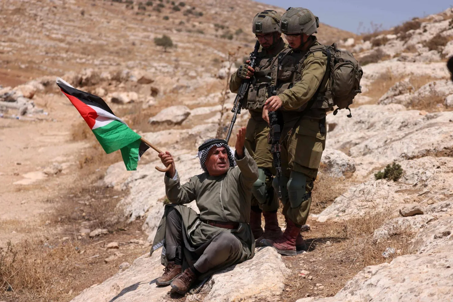 فلسطيني برفع علم بلاده احتجاجاً على إقامة مستوطنة إسرائيلية خارج قرية بيت دجن شرق مدينة نابلس (أ.ف.ب)