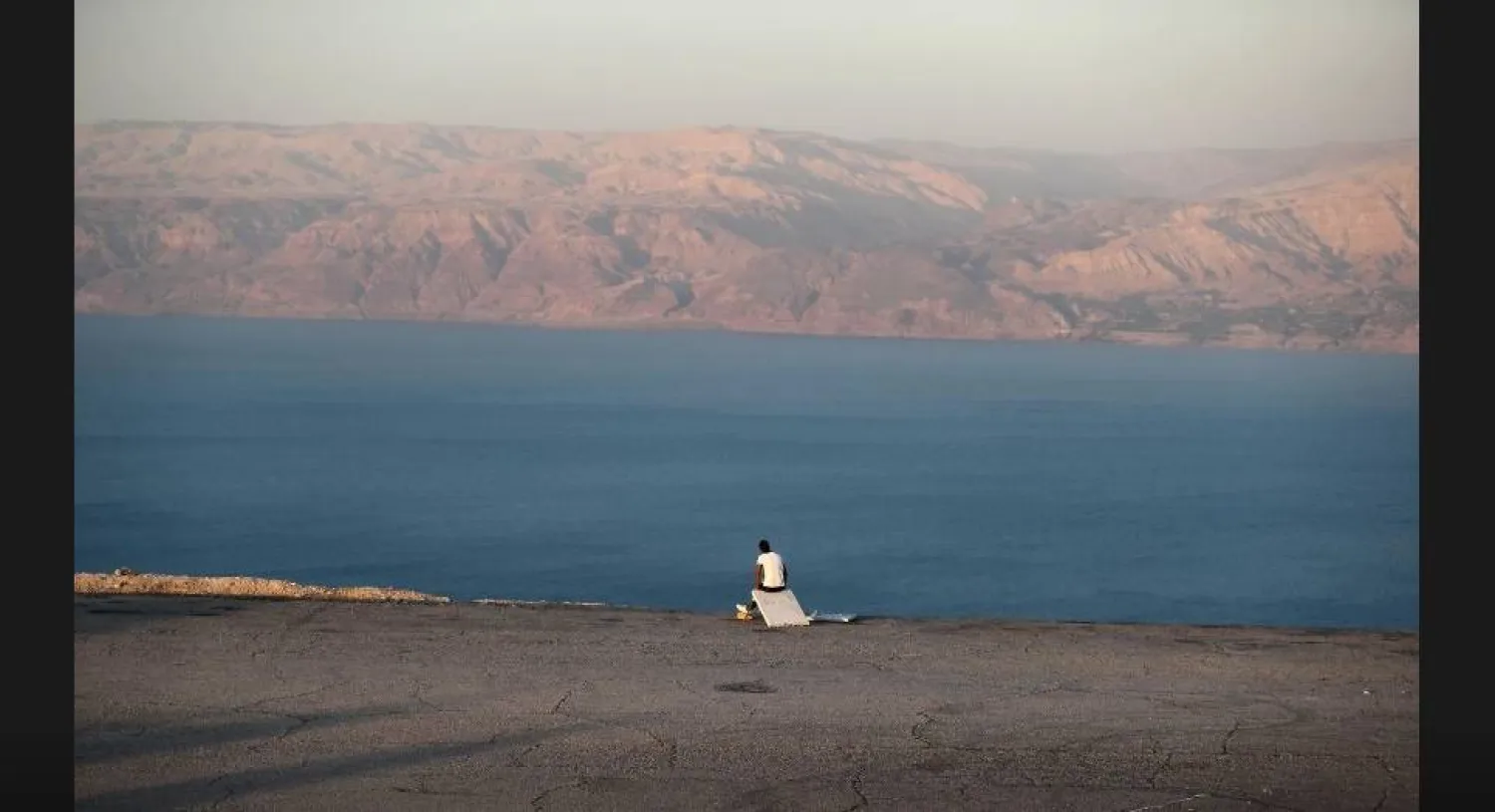 رجل يجلس على شاطئ البحر الميت في الضفة الغربية (رويترز)