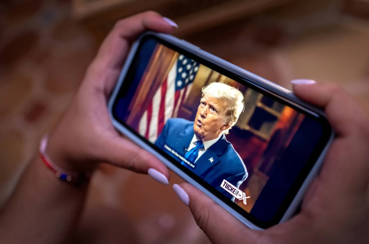 أميركية تتابع على هاتفها مقابلة ترمب على منصة «إكس» فيما تغيب عن المناظرة بين المرشحين الجمهوريين الأربعاء (إ.ب.أ)