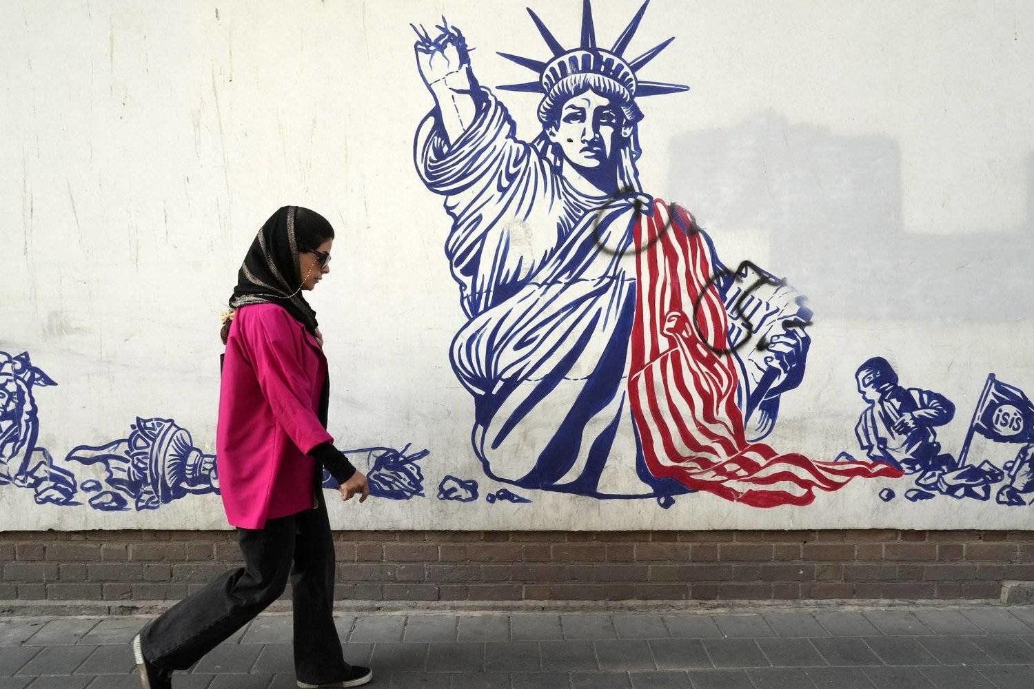 An Iranian woman walks past an anti-US mural on the wall of the former US Embassy in Tehran. (AP)  