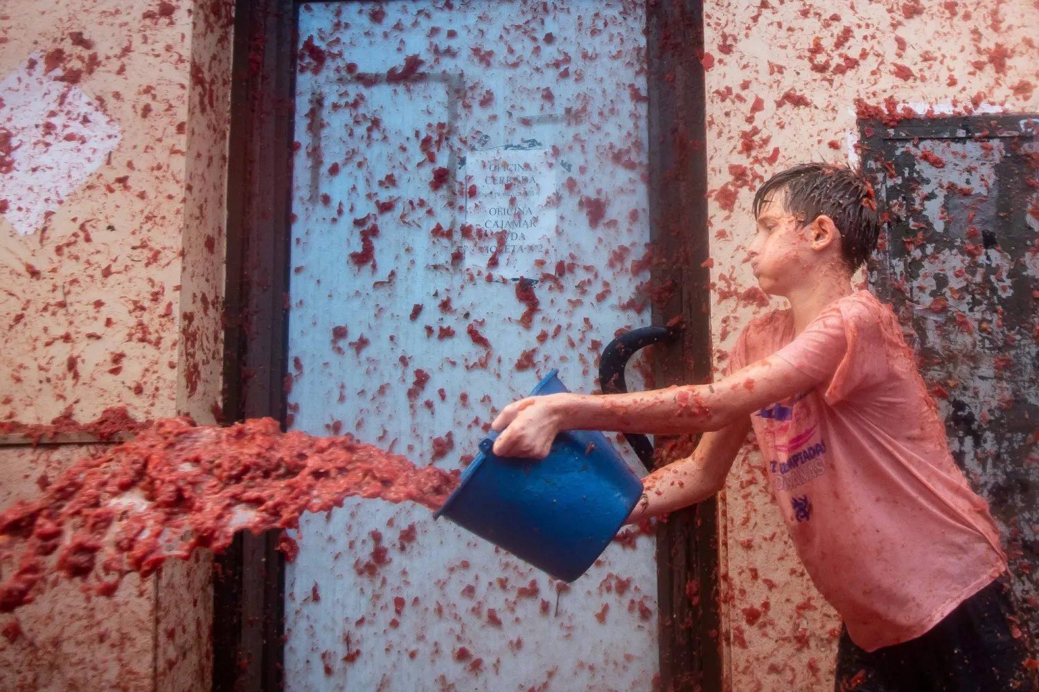 A reveler uses a bucket to hurl crushed tomatoes during the "Tomatina" annual food-battle in the Spanish eastern town of Bunol, on August 30, 2023. (Photo by Jose Miguel FERNANDEZ / AFP)