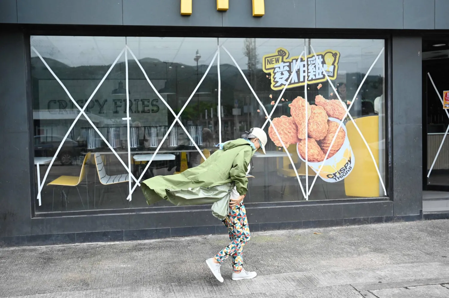 A woman walks past a closed fast food outlet with windows taped up for protection on Lantau island in Hong Kong on September 1, 2023, hours before the expected arrival of Super Typhoon Saola. (Photo by Peter PARKS / AFP)