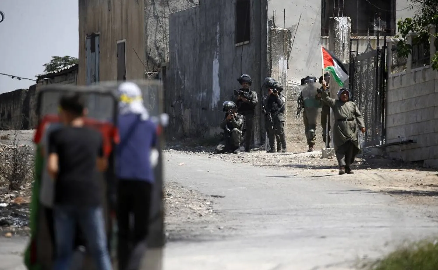A man waves a Palestinian flag as Palestinian protesters take cover behind shields during clashes with Israeli troops after a demonstration against Israel's settlements on the lands of Kafr Qadoum village, near the West Bank city of Nablus, 25 August 2023. (EPA)