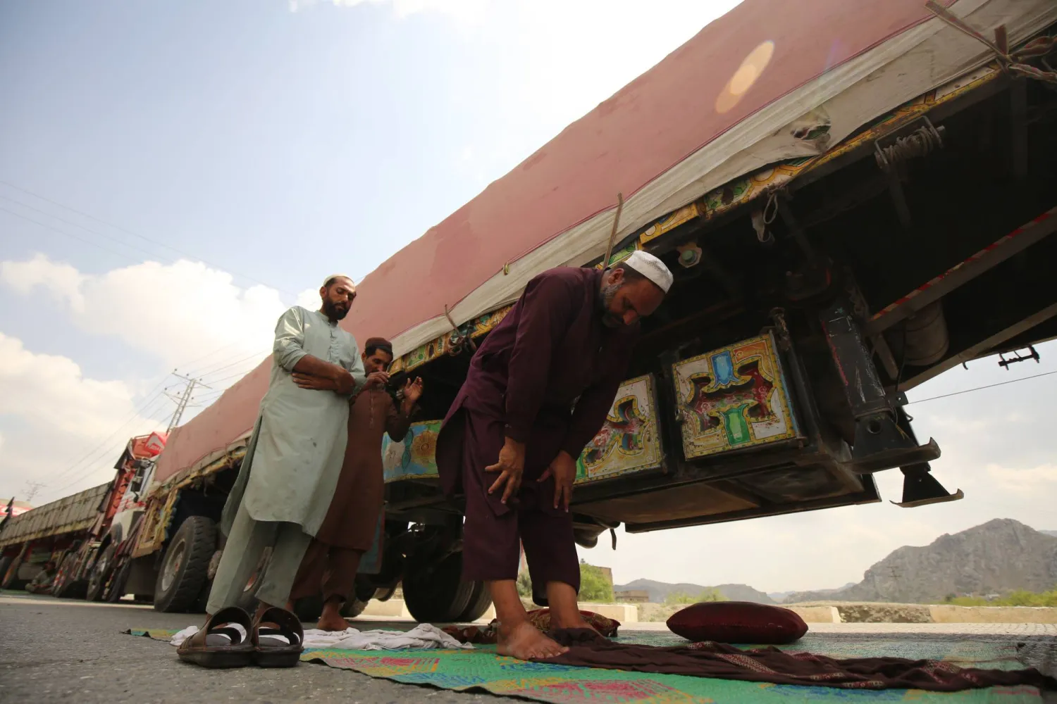 سائقو الشاحنات يؤدون صلاة الظهر بجانب شاحناتهم المتوقفة التي تحمل بضائع متجهة إلى أفغانستان بينما ينتظرون فتح الحدود بعد اشتباكات بين قوات الأمن الباكستانية والأفغانية في تورخام (إ.ب.أ)