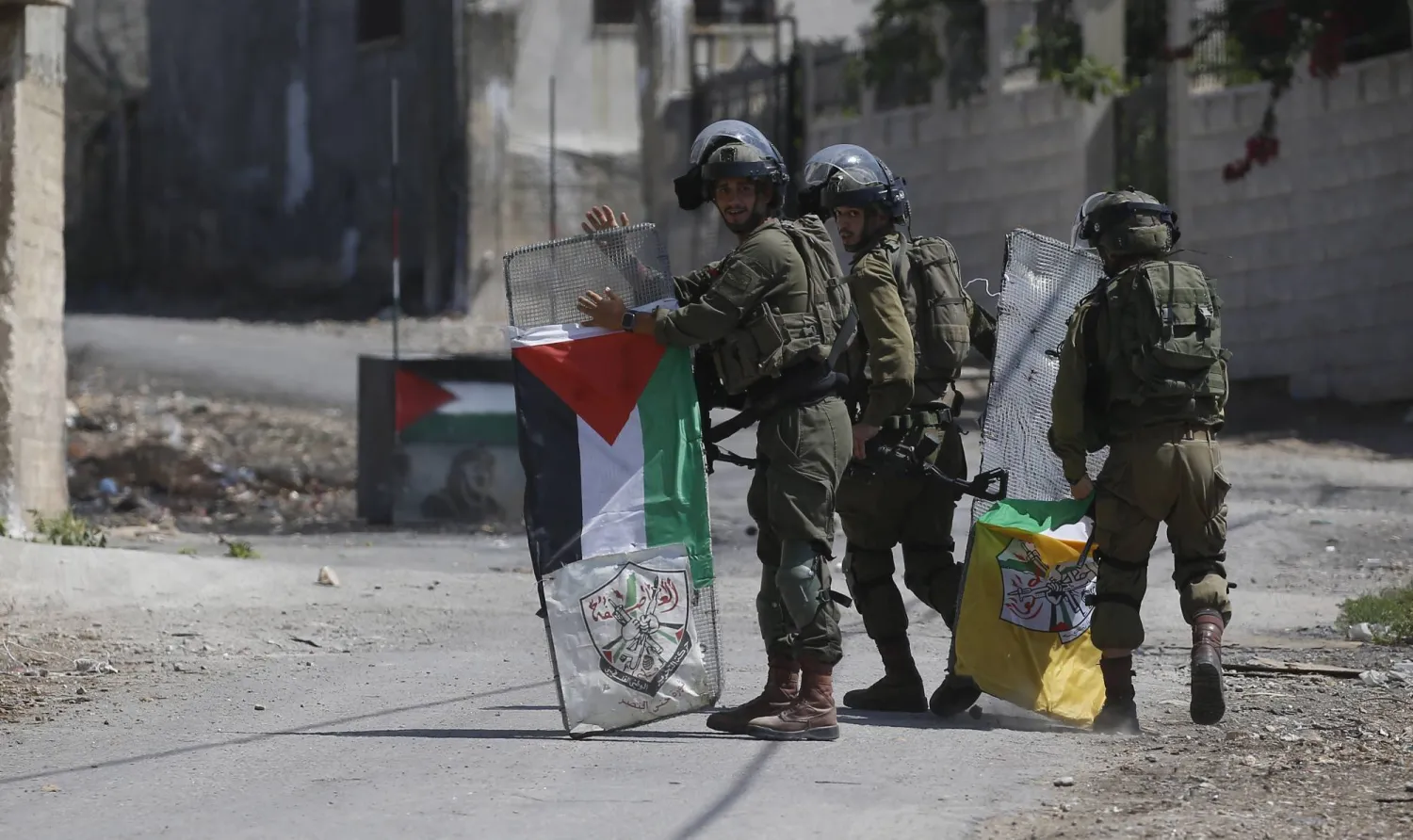 جنود إسرائيليون ينزعون علم فلسطين بعد أن استخدمه فلسطينيون خلال احتجاجات في الضفة الغربية أمس (إ.ب.أ)