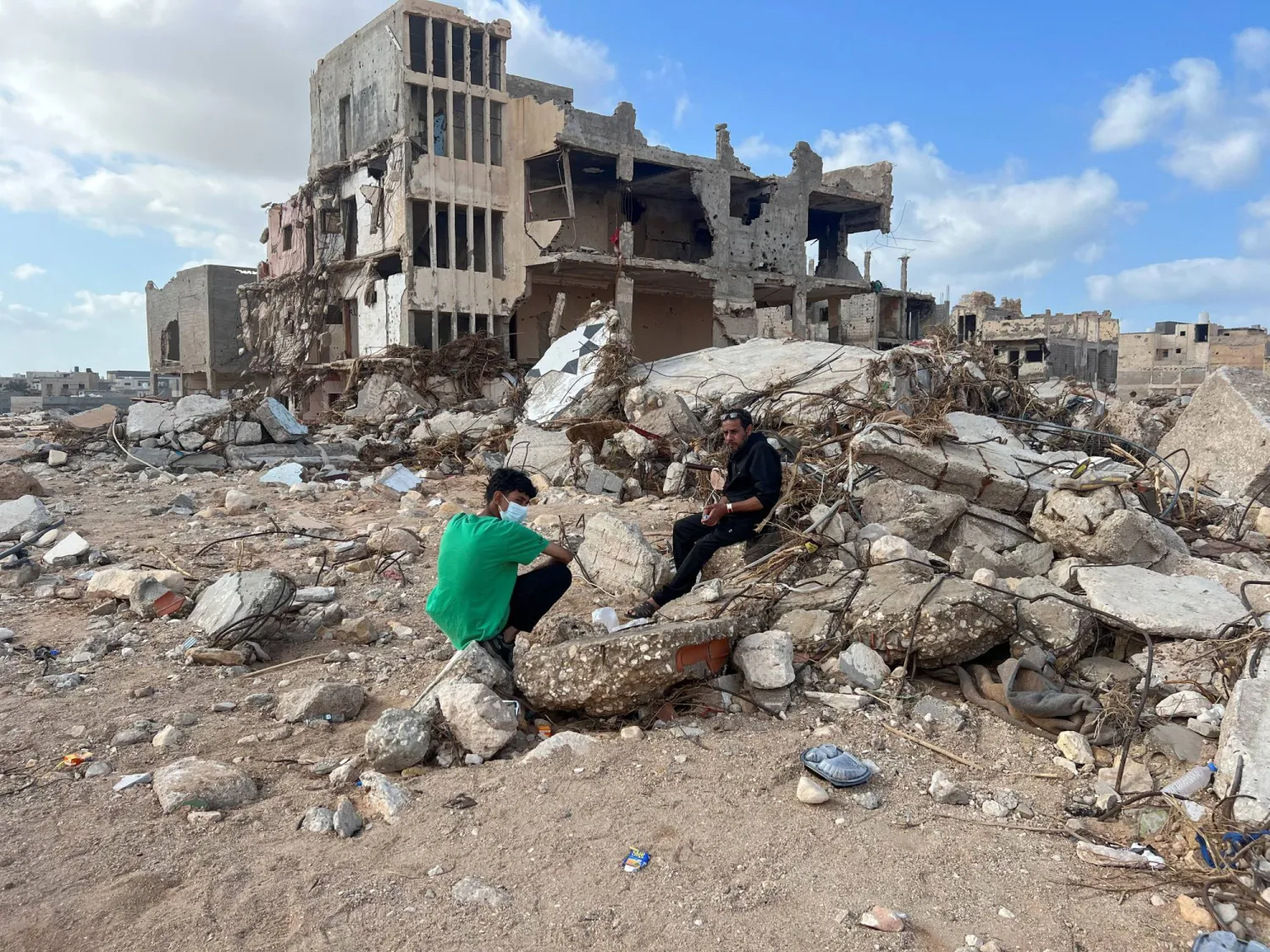 مواطنان يجلسان أمام بقايا منزل تهدم في مدينة درنة الليبية (رويترز)