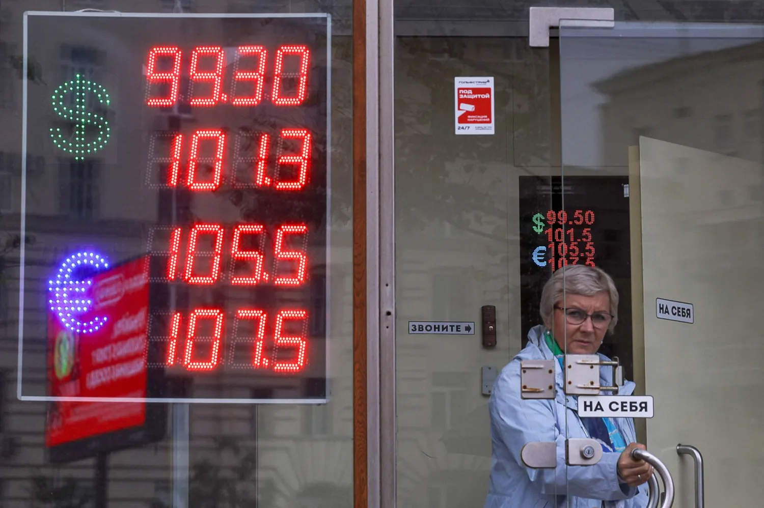 سيدة تخرج من إحدى نقاط الصرافة في العاصمة الروسية موسكو بينما تظهر الشاشة تراجع الروبل إلى 101 مقابل الدولار (رويترز)