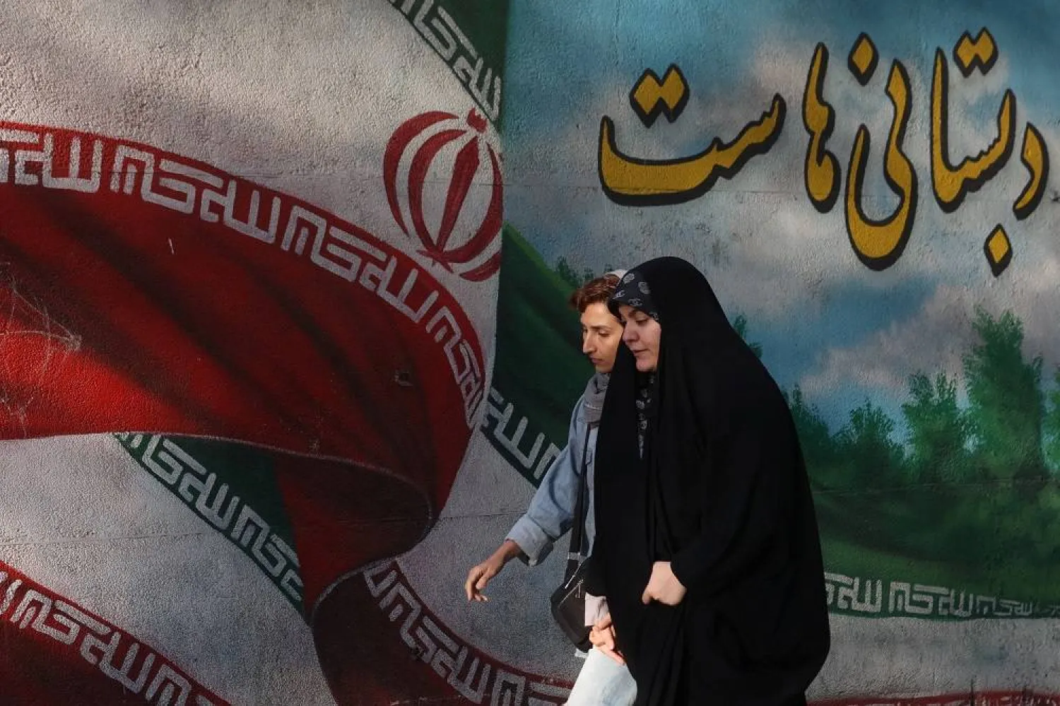 Iranian women walks past a mural with a picture of the Iranian flag on a street in Tehran, Iran, October 6, 2023. Majid Asgaripour/WANA (West Asia News Agency) via Reuters. 