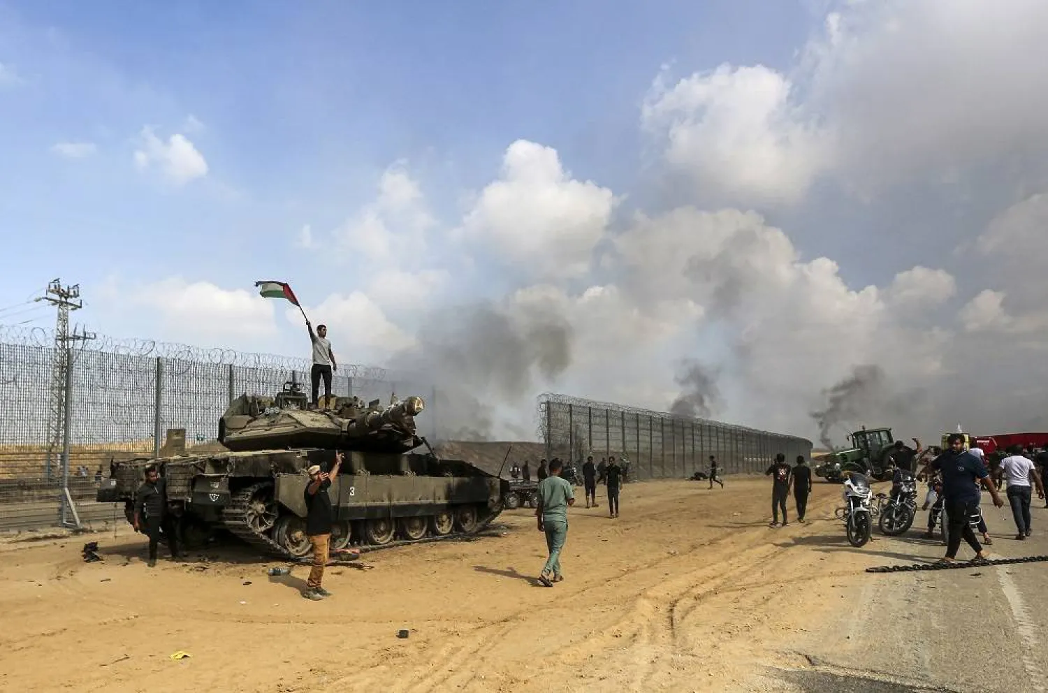 Palestinians wave their national flag and celebrate by a destroyed Israeli tank at the Gaza Strip fence east of Khan Younis southern Saturday, Oct. 7, 2023. (AP)