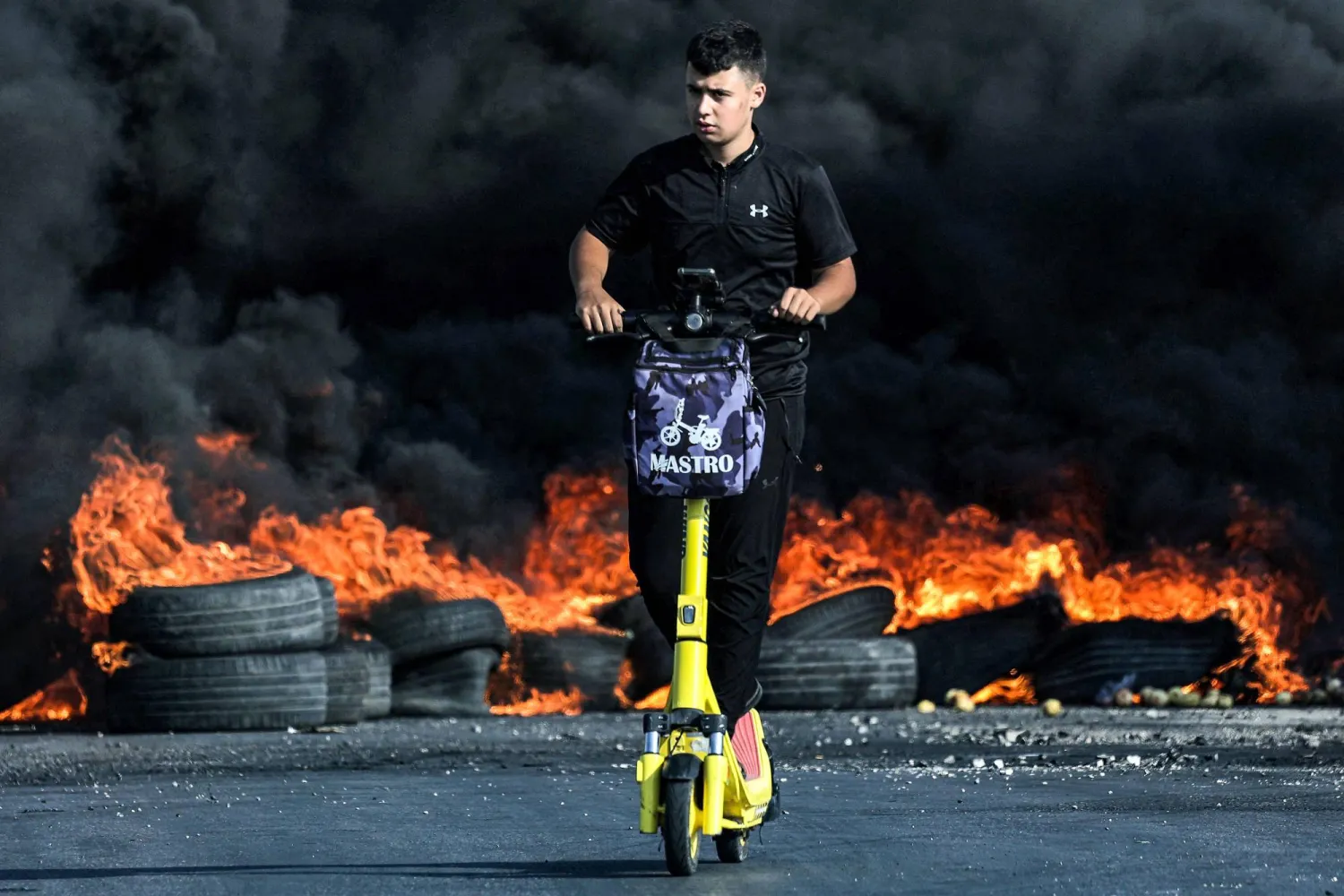 A Palestinian demonstrator rides a scooter past burning tires during clashes with Israeli soldiers in the city of Ramallah in the occupied West Bank on October 8, 2023. (Photo by Jaafar ASHTIYEH / AFP)
