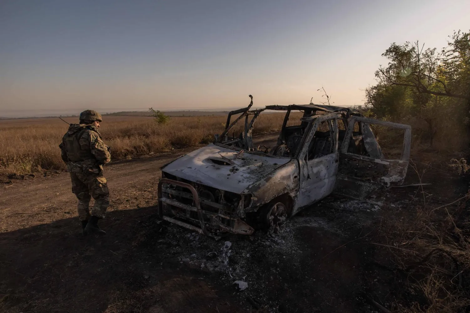 A Ukrainian soldier of the 65th Mechanized Brigade walks past a destroyed car, next to the trenches built by Russian forces, and that were captured by the Ukrainian army, near the frontline village of Robotyne, in the Zaporizhzhia region, on October 1, 2023, amid the Russian invasion of Ukraine. (Photo by Roman PILIPEY / AFP)