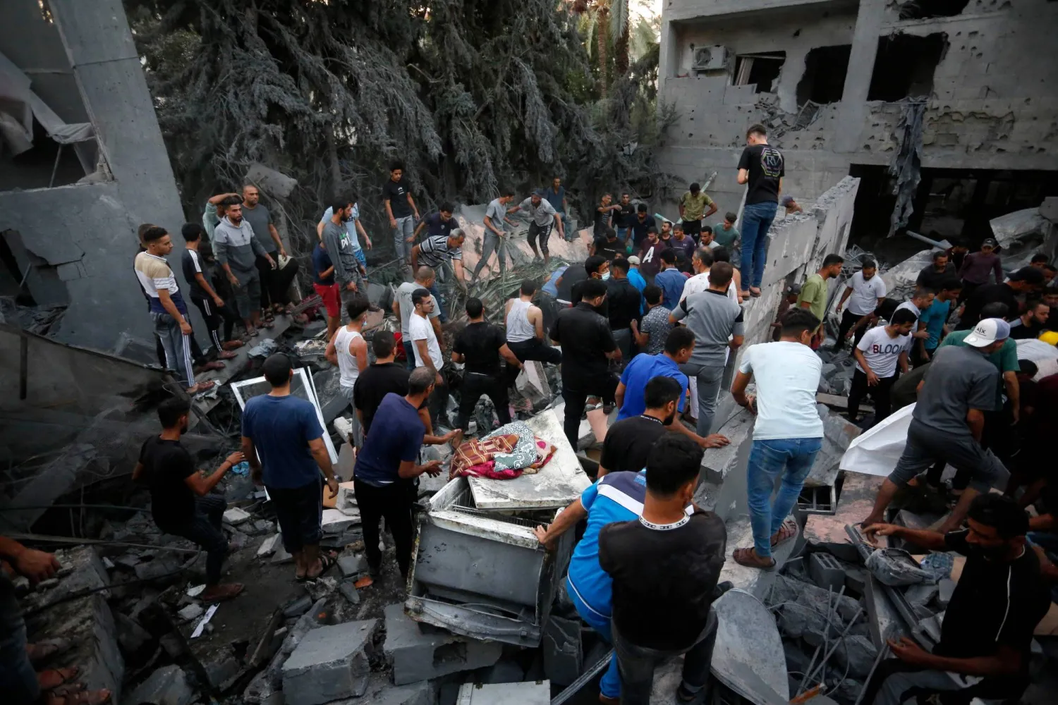 أشخاص يبحثون عن الضحايا والناجين في أعقاب غارة إسرائيلية على بلدة دير البلح بوسط قطاع غزة (أ.ف.ب)