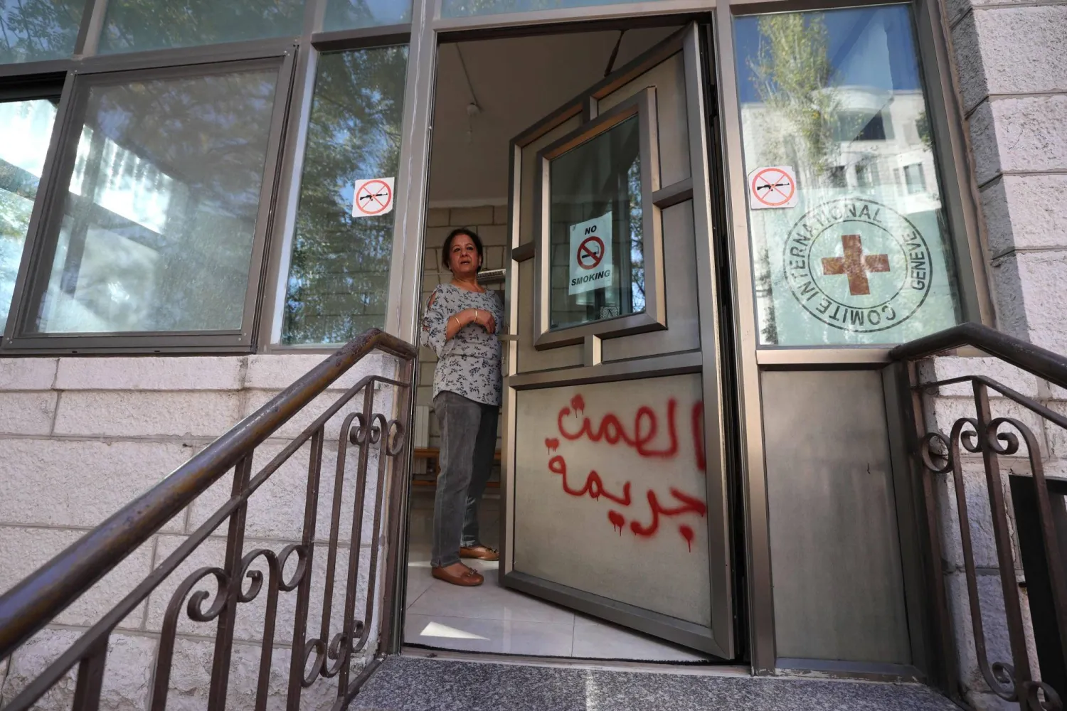 موظفة تدخل مكاتب الصليب الأحمر بعد أن خط نشطاء فلسطينيون عبارة «الصمت جريمة» في رام الله بالضفة الغربية (أ.ف.ب)