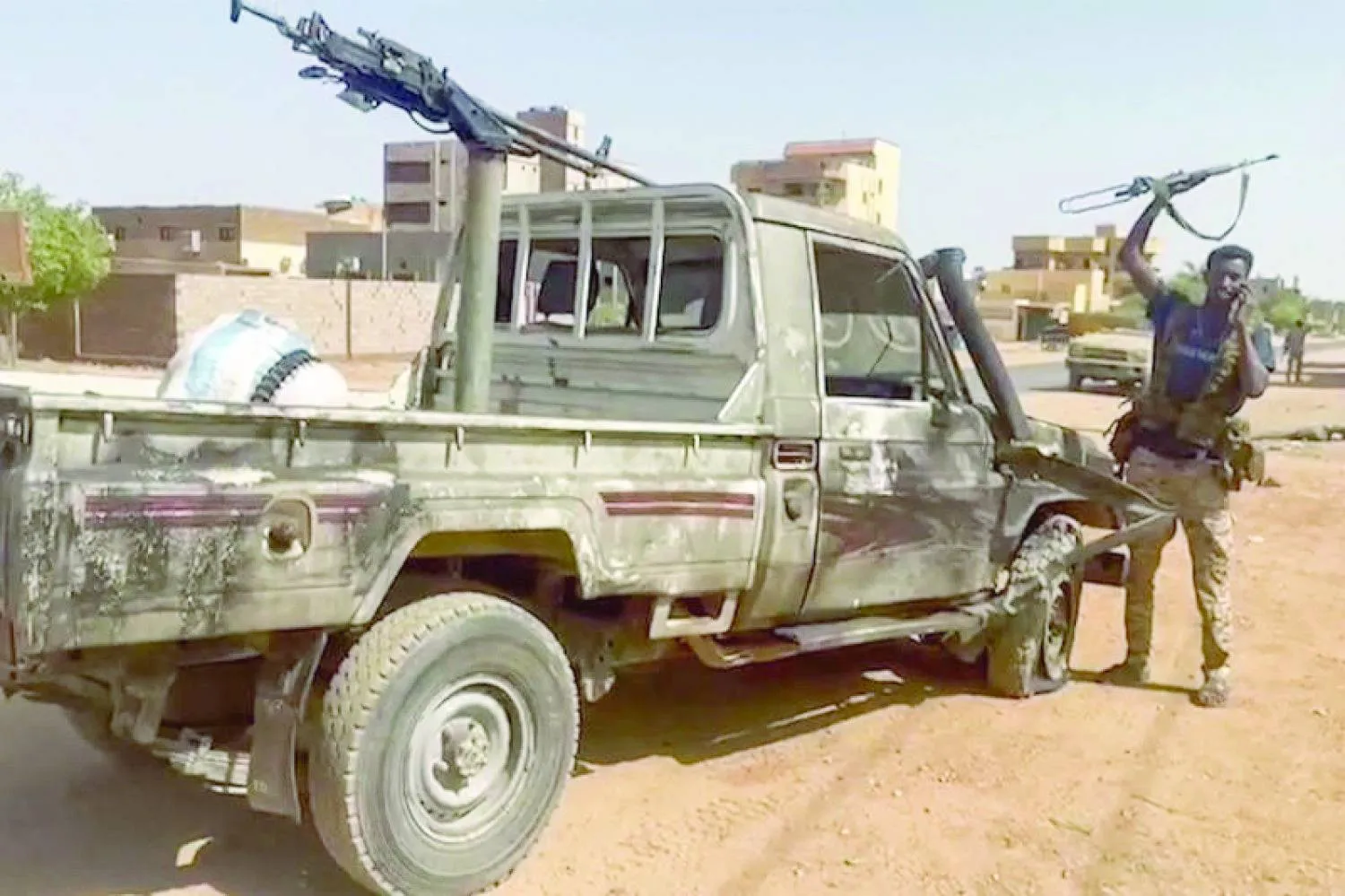 مقاتل يلوِّح ببندقية وهو يقف بجانب مركبة معطوبة في حي النيل بالخرطوم الكبرى (أ.ف.ب)