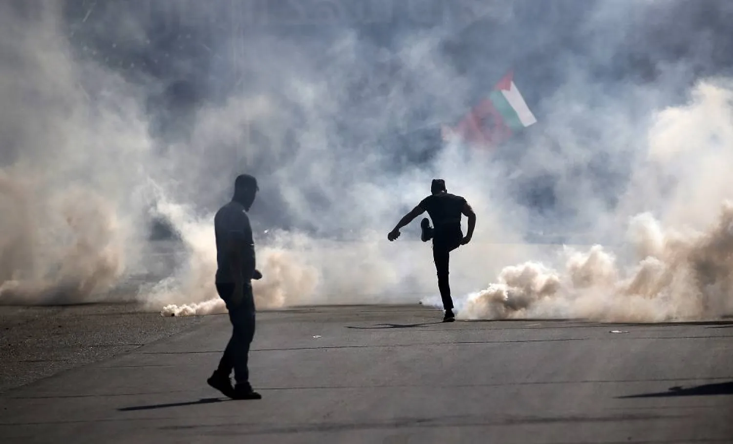 A Palestinian man kicks away a tear gas canister during clashes with Israeli forces in the West Bank city of Nablus, 13 October 2023. (EPA)