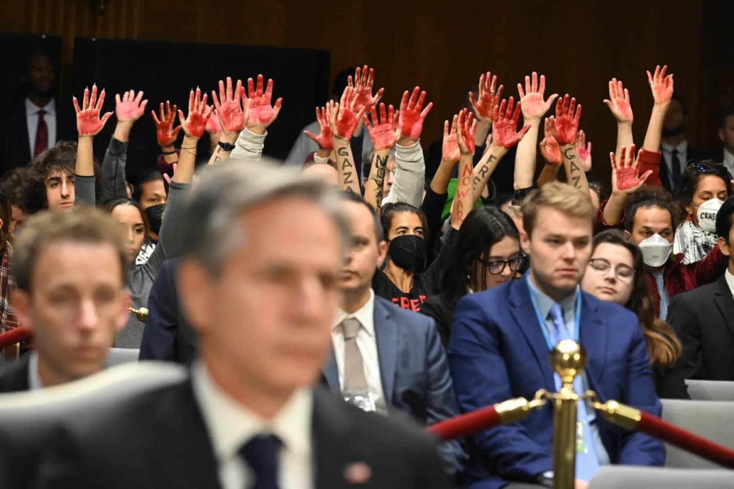 ABD Dışişleri Bakanı Antony Blinken Kongre'de açıklamalarda bulunurken göstericiler üzerinde ‘Gazze’ yazan kırmızıya boyanmış ellerini kaldırdı. (AFP/Saul Loeb)