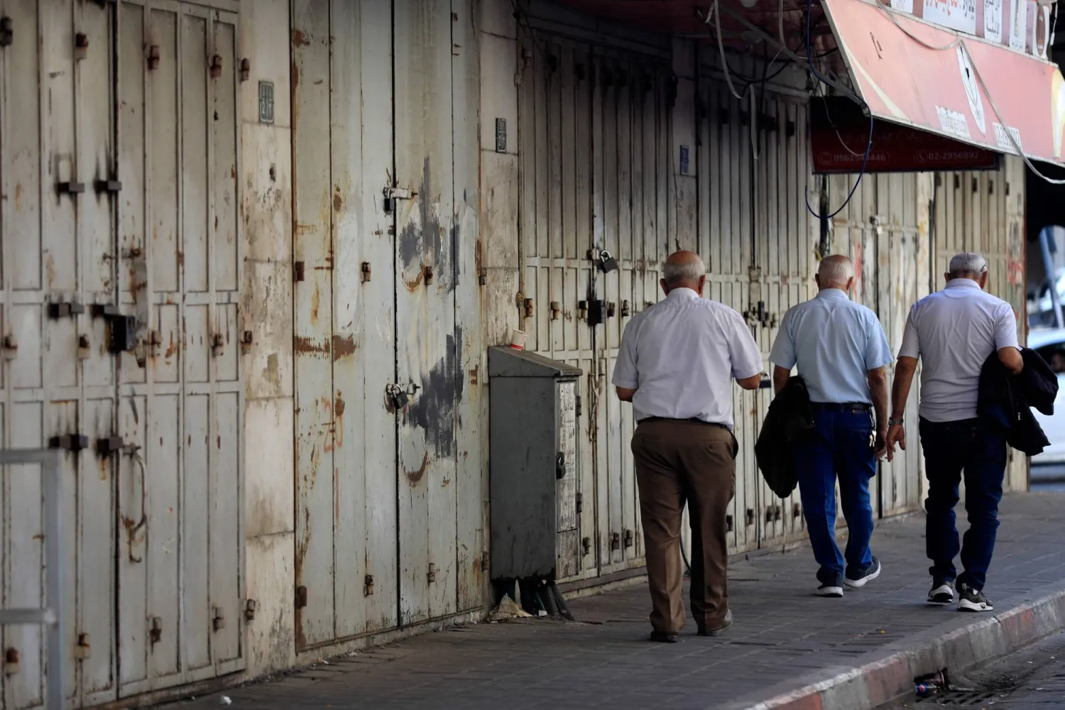 أشخاص يسيرون أمام المتاجر المغلقة في أعقاب الدعوة إلى إضراب عام لدعم الفلسطينيين في قطاع غزة، في مدينة رام الله بالضفة الغربية المحتلة (أ.ف.ب)