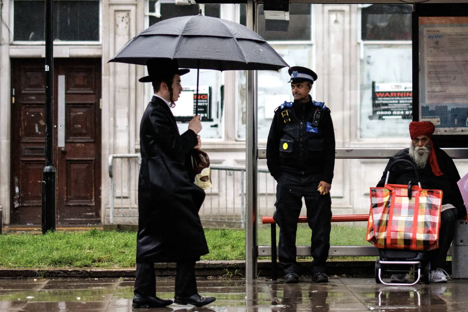 يهودي أرثوذكسي يمر قرب شرطي في منطقة ستامفورد هيل بلندن (إ.ب.أ)