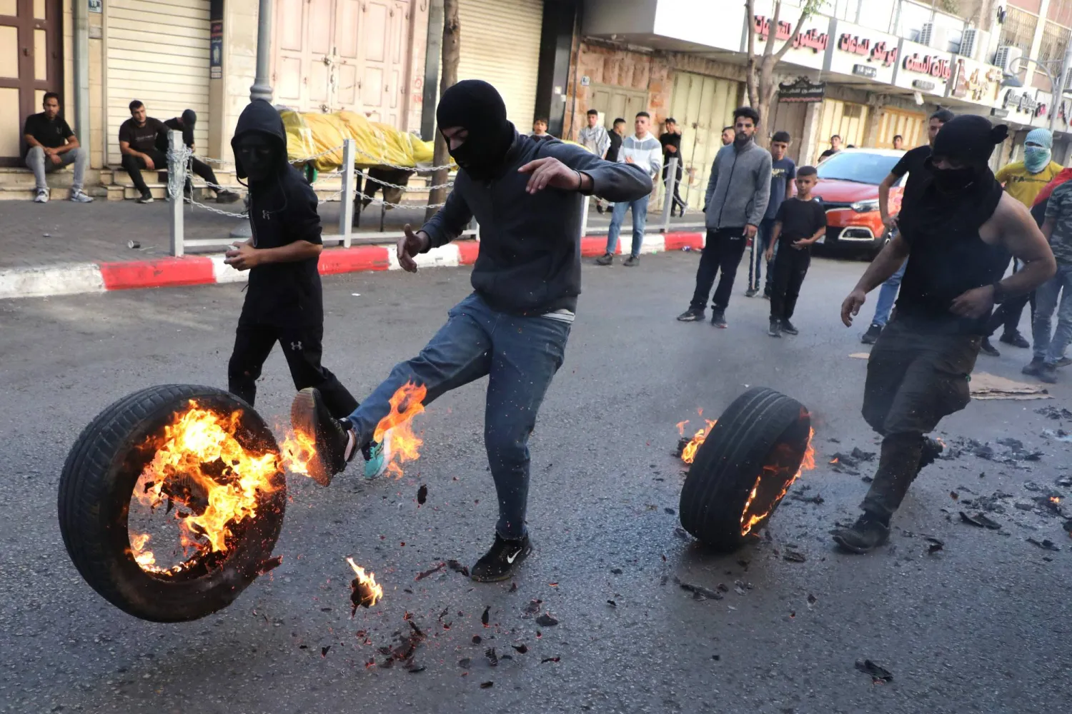 فلسطينيون يركلون إطارات مشتعلة خلال مواجهات مع قوات الأمن الإسرائيلية في مدينة الخليل بالضفة الغربية (أ.ف.ب)