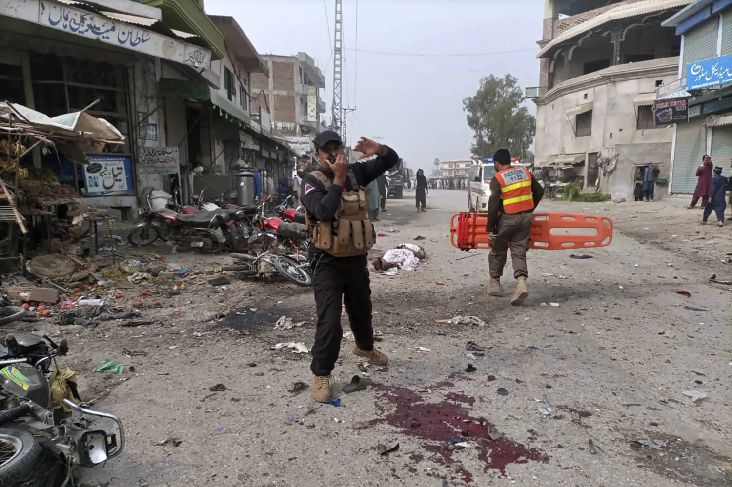 A police officer talks on his wireless set as a rescue worker moves towards a victim at the site of bomb blast in Dera Ismail Khan, Pakistan, Friday, Nov. 3, 2023. (AP Photo/Irfan Mughal)