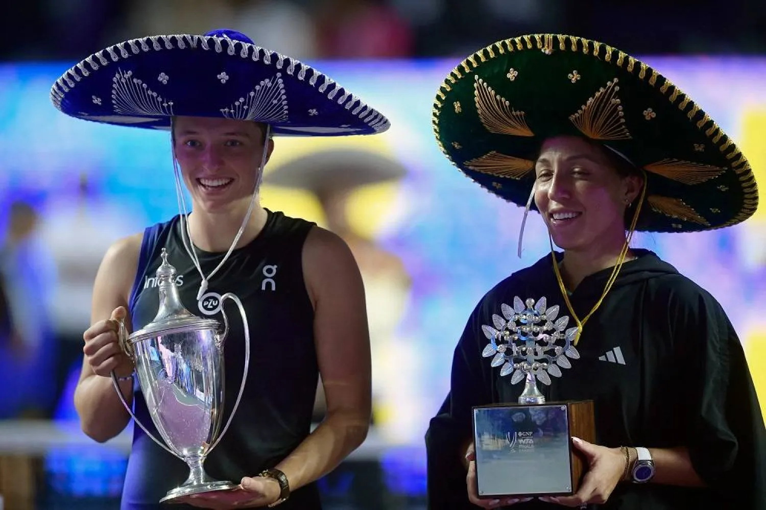 Poland's Iga Swiatek (L) and US' Jessica Pegula wearing Mexican hats, pose on the podium with their trophies during the awards ceremony at the end of the WTA Finals Championship women's singles final tennis match in Cancun, Mexico on November 6, 2023. (AFP)