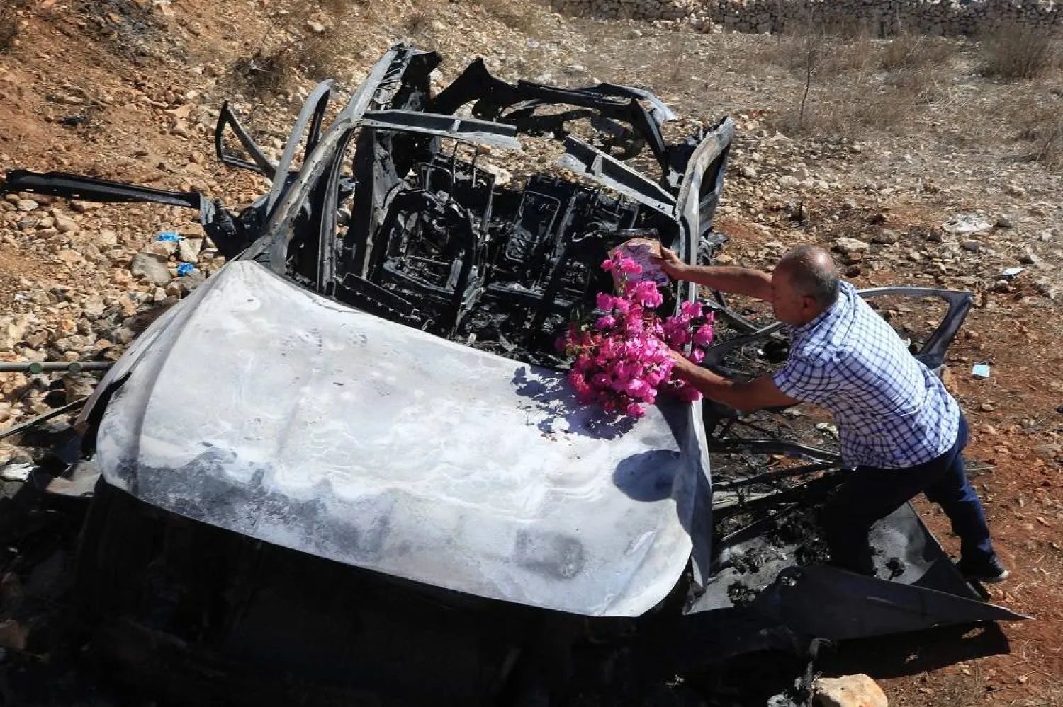 A Lebanese man puts flowers on the wreckage of a vehicle in which his relatives were killed during an Israeli strike in southern Lebanon near the border with Israel, on November 6, 2023. (AFP)