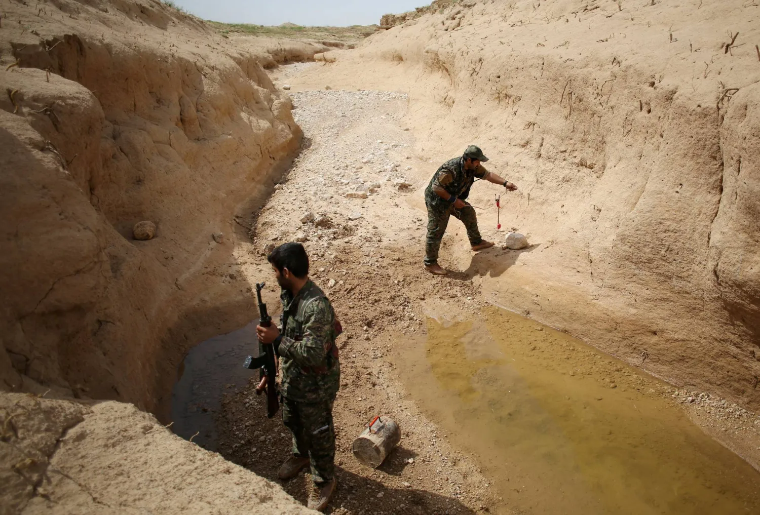عنصران من وحدات المقاومة في سنجار المقربة من حزب العمال الكردستاني يزرعون متفجرات في قرية قرب سنجار (رويترز)