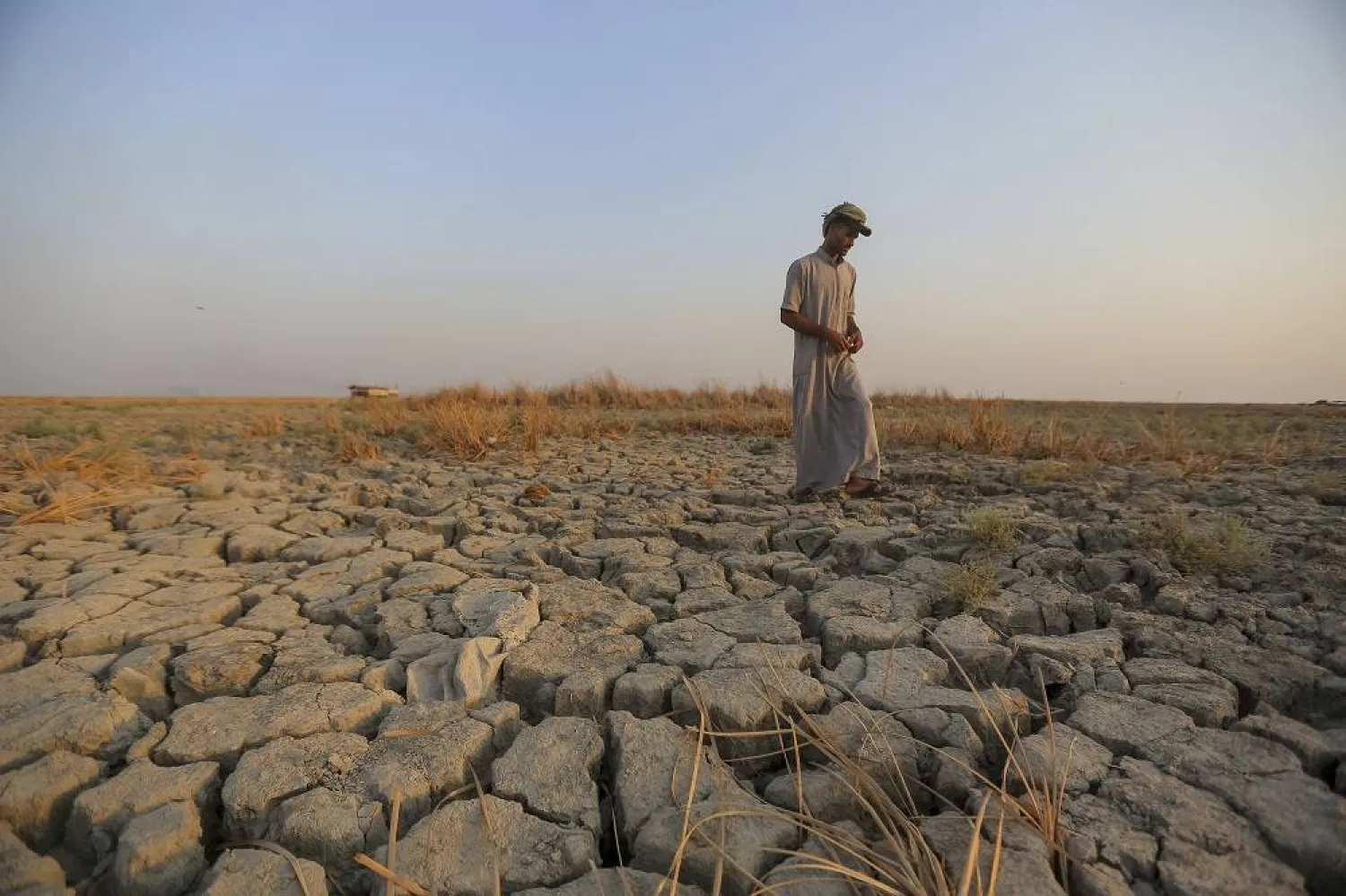 A fisherman walks across a dry patch of land in the marshes in Dhi Qar province, Iraq, Sept. 2, 2022. (AP)
