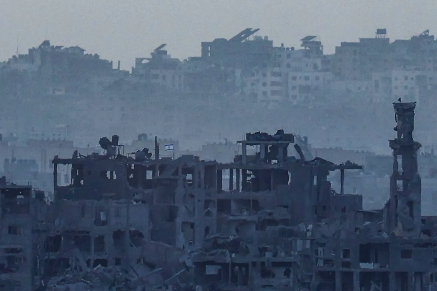 عَلَم إسرائيلي يرفرف فوق أنقاض مبنى مدمَّر بجوار قبة ومئذنة مسجد في شمال قطاع غزة 9 نوفمبر 2023 (أ.ف.ب)