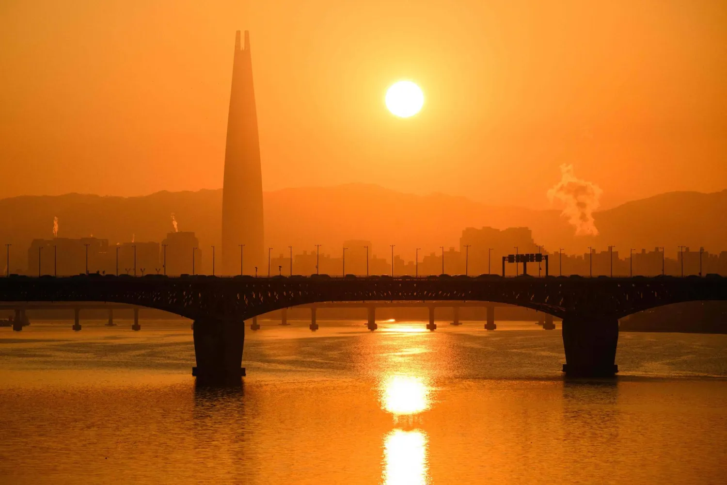 A general view shows the Lotte Tower (L) and the sun rising over the Han river in Seoul on November 22, 2023. (Photo by ANTHONY WALLACE / AFP)