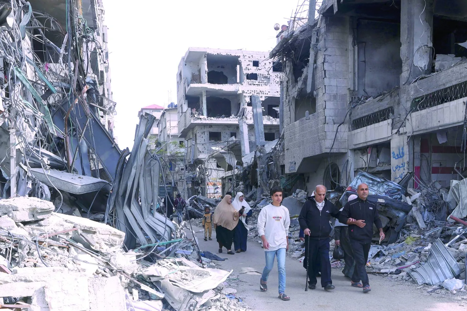 Palestinians walk by buildings destroyed in the Israeli bombardment of the Gaza Strip in Nusseirat refugee camp, central Gaza Strip, Saturday, Nov. 25, 2023. (AP Photo/Adel Hana)