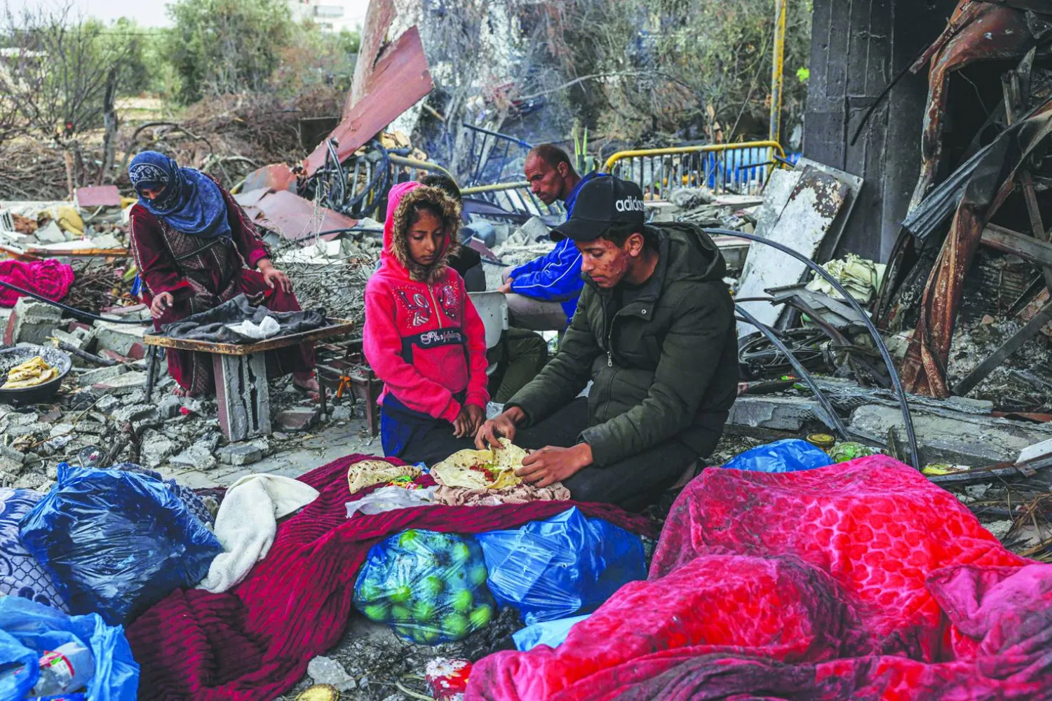 
غزيون يتناولون الطعام وسط الدمار الذي خلفه القصف الإسرائيلي في قرية خزاعة شرق خان يونس أمس (أ.ف.ب)