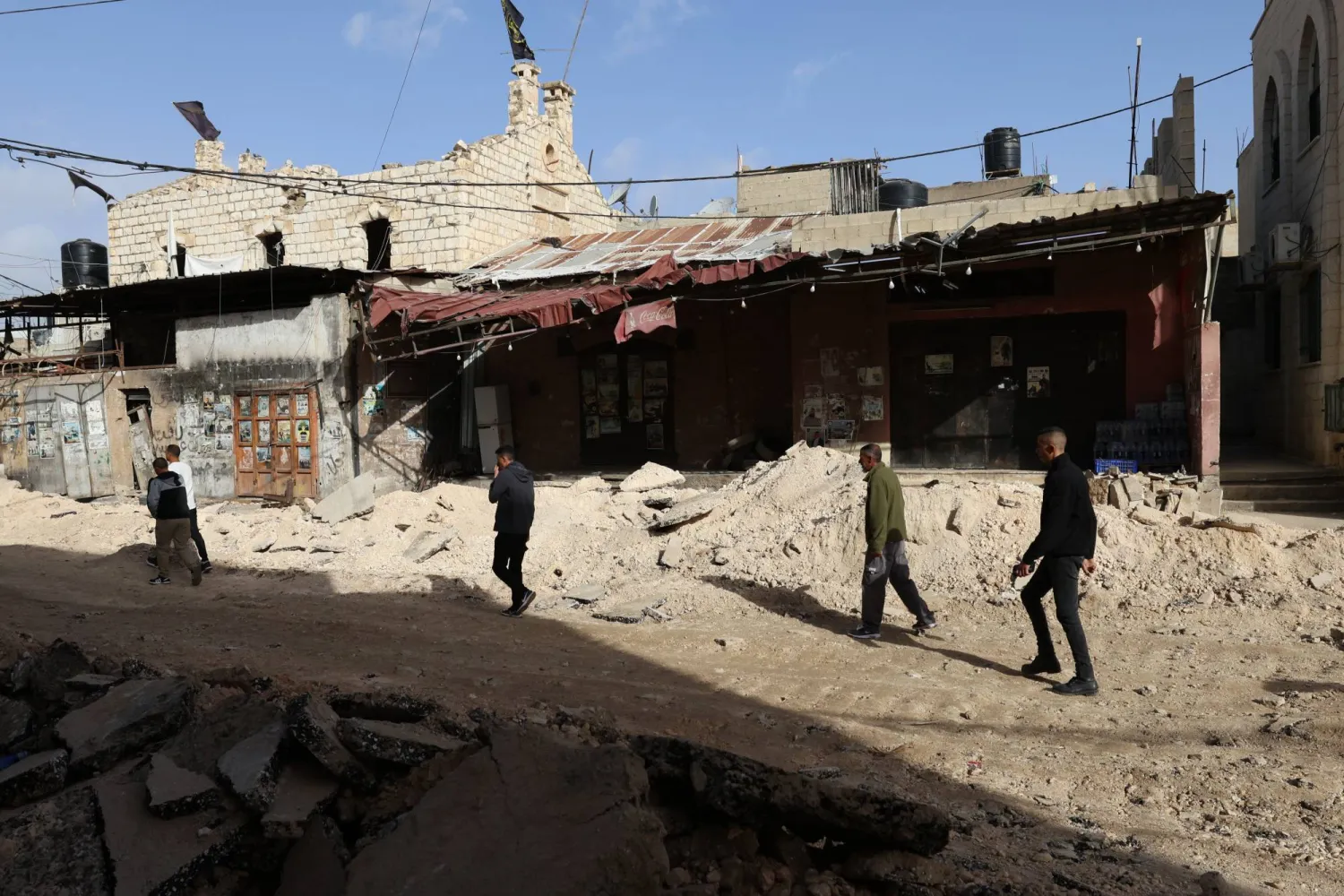 أشخاص يسيرون وسط الأنقاض في أحد الشوارع بعد عملية إسرائيلية بمخيم جنين للاجئين بالضفة الغربية (إ.ب.أ)