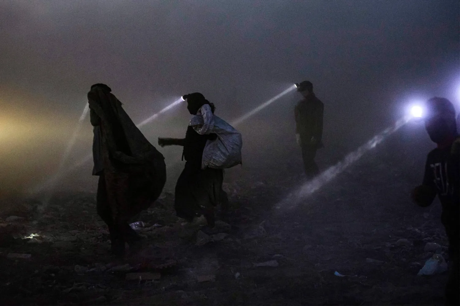 People equipped with searchlights scan for recyclable material for resale at a landfill in Iraq's southern city of Basra late at night on June 22, 2023. (Photo by Hussein Faleh / AFP) / AFP PICTURES OF THE YEAR 2023
