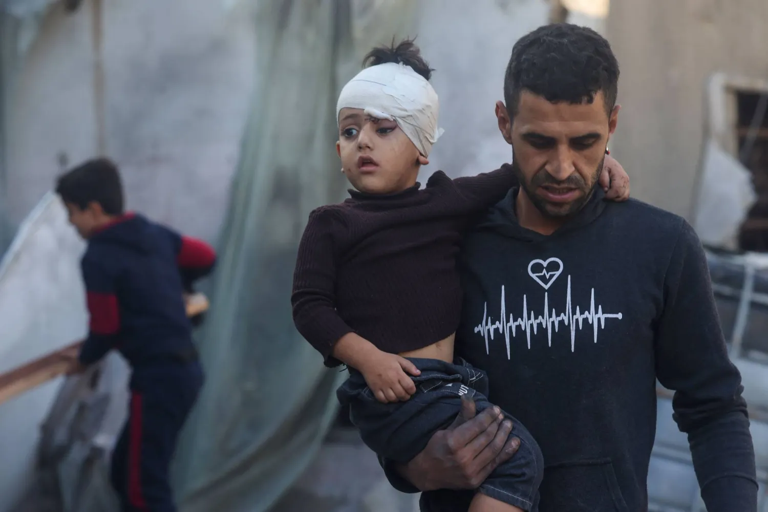 فلسطيني يحمل طفلاً أصيب أثناء القصف الإسرائيلي على رفح بجنوب قطاع غزة (أ.ف.ب)