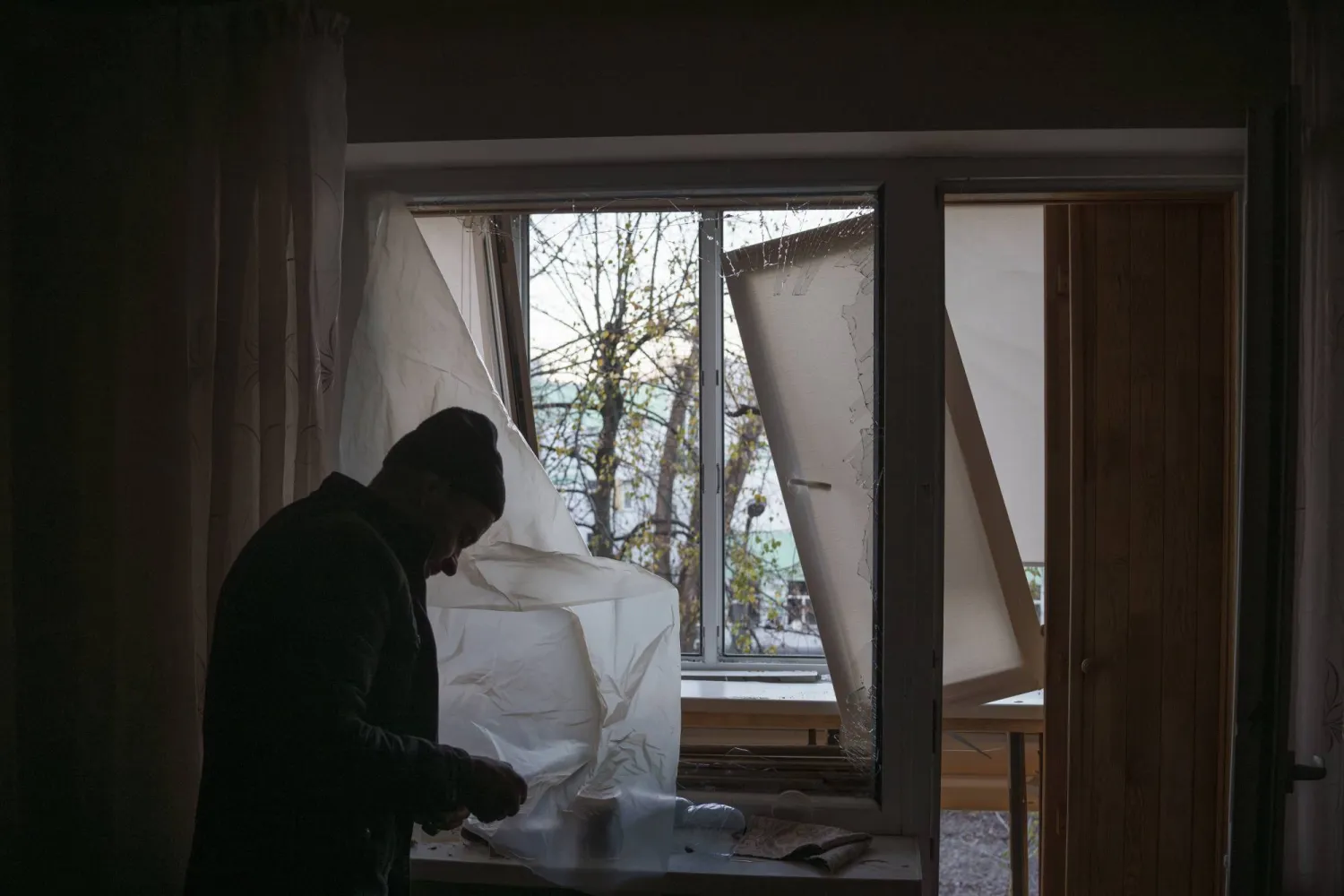 FILE - A man uses plastic to cover a broken window in his apartment following a Russian drone attack in Kyiv, Ukraine, Saturday, Nov. 25, 2023. (AP Photo/Felipe Dana, File)