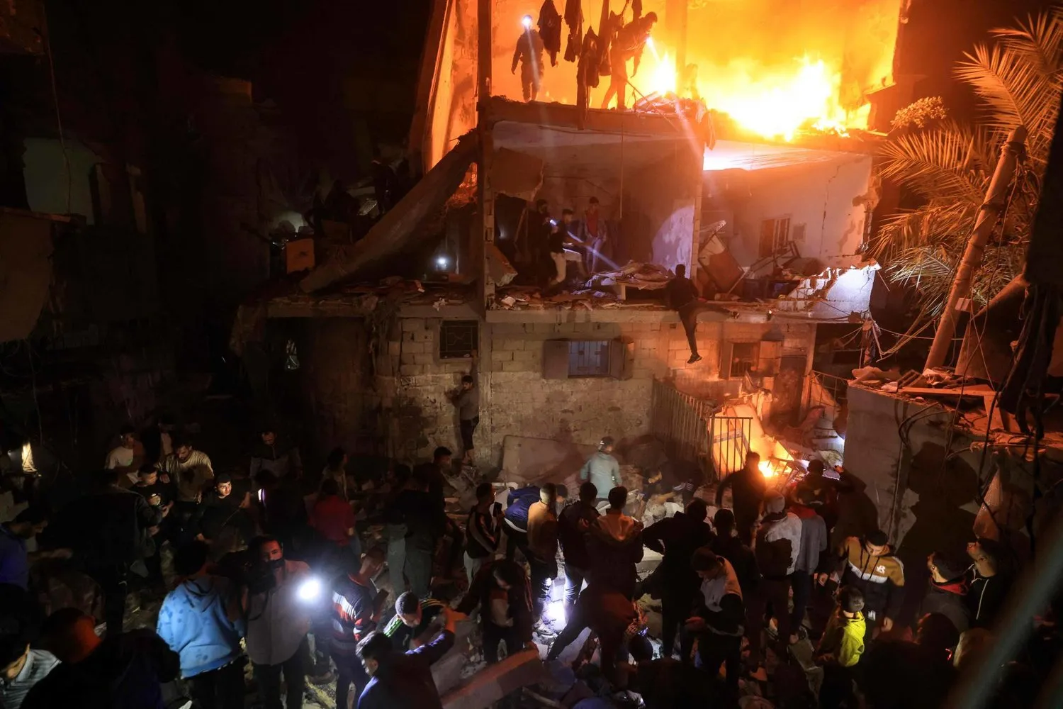 İsrail’in Gazze Şeridi’nin güneyindeki Refah’a düzenlediği hava saldırısının ardından yanan bir binanın enkazı arasında kurbanlar aranıyor (AFP)