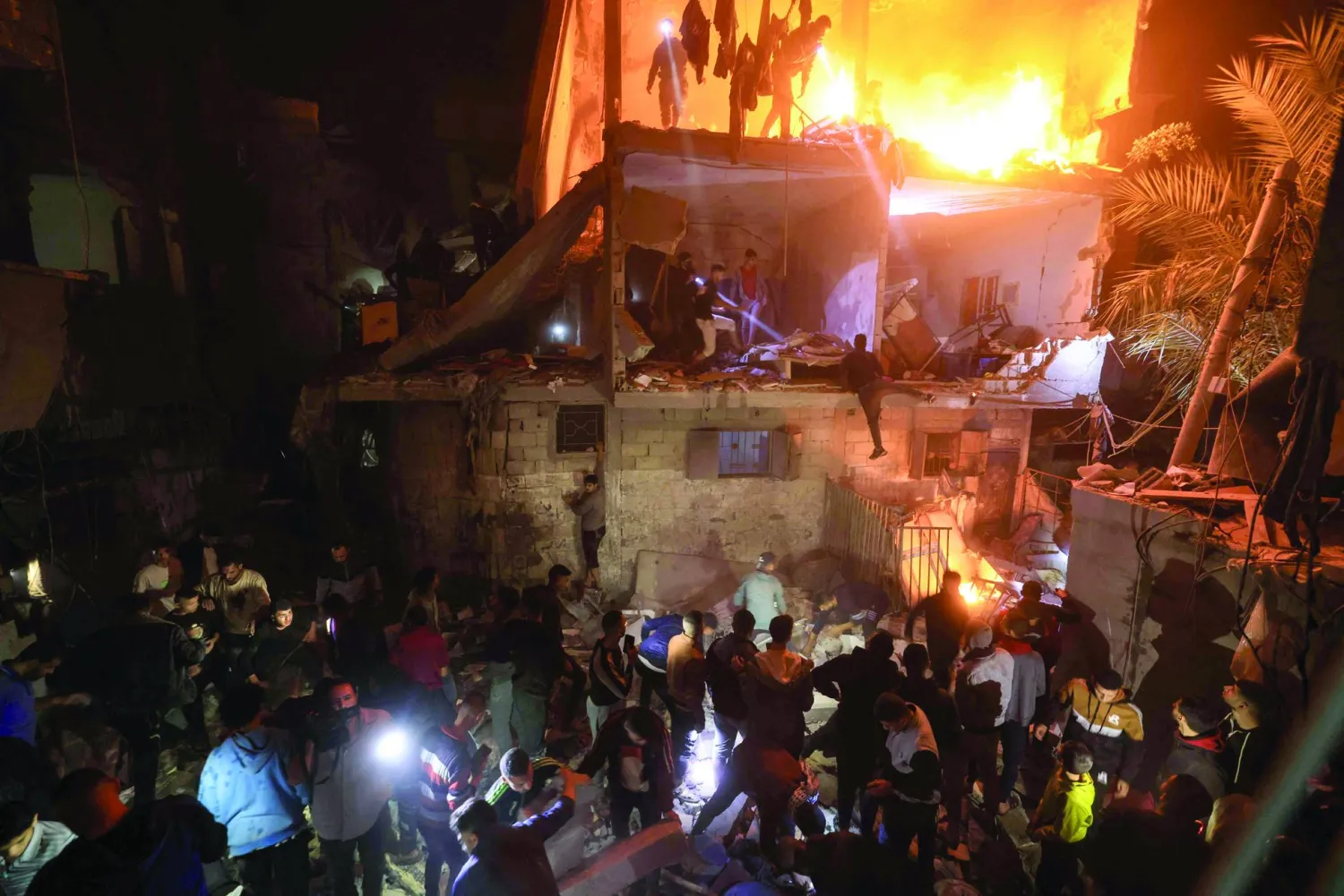 
بحث عن الضحايا وسط أنقاض مبنى مشتعل في أعقاب غارة إسرائيلية على رفح جنوب قطاع غزة (أ.ف.ب)