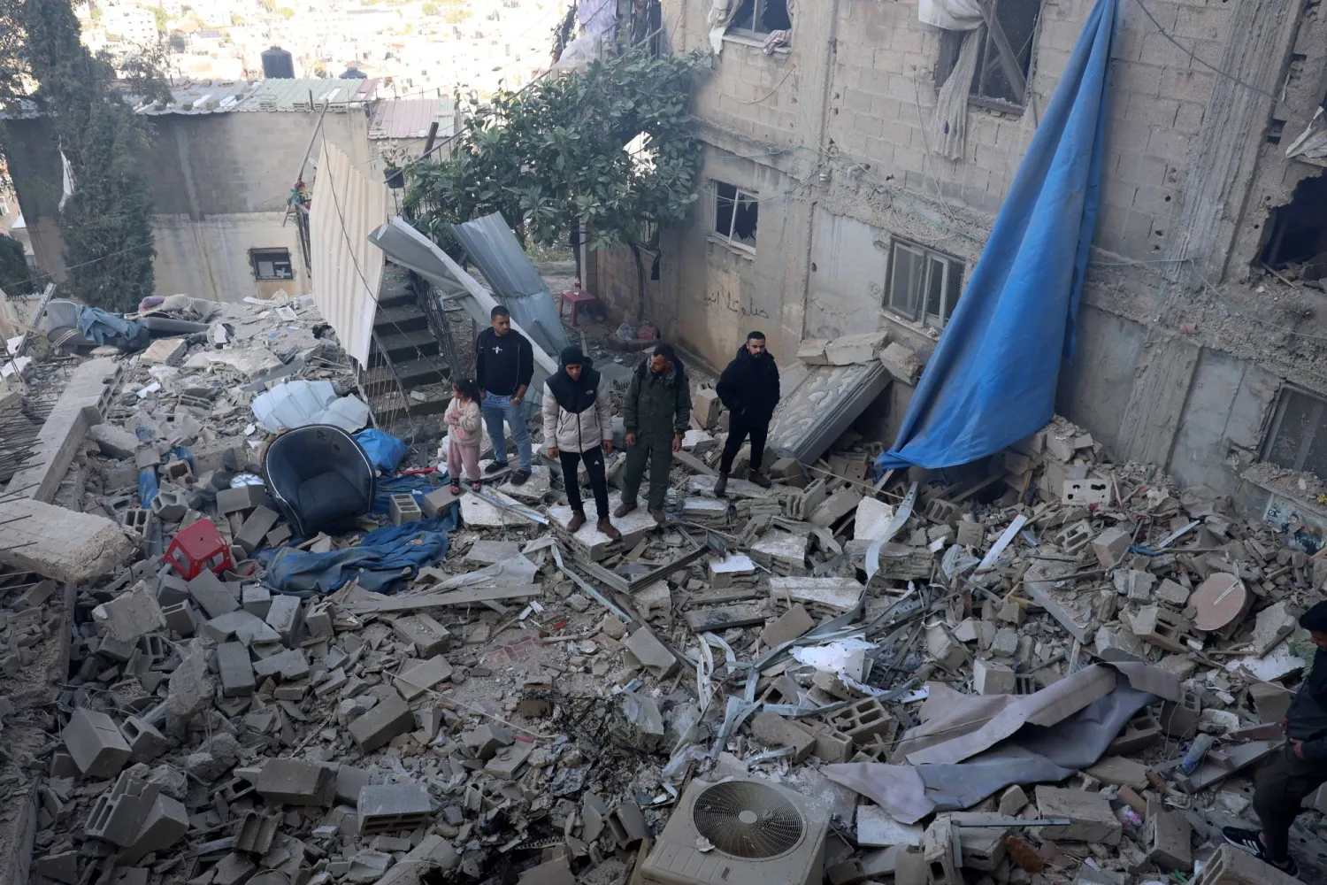 أشخاص يقفون في محيط منزلهم المدمر إثر العدوان على مخيم جنين (إ.ب.أ)